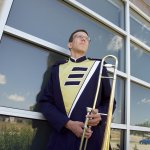 Luke in marching band uniform holding trombone looking up into the blue sky.